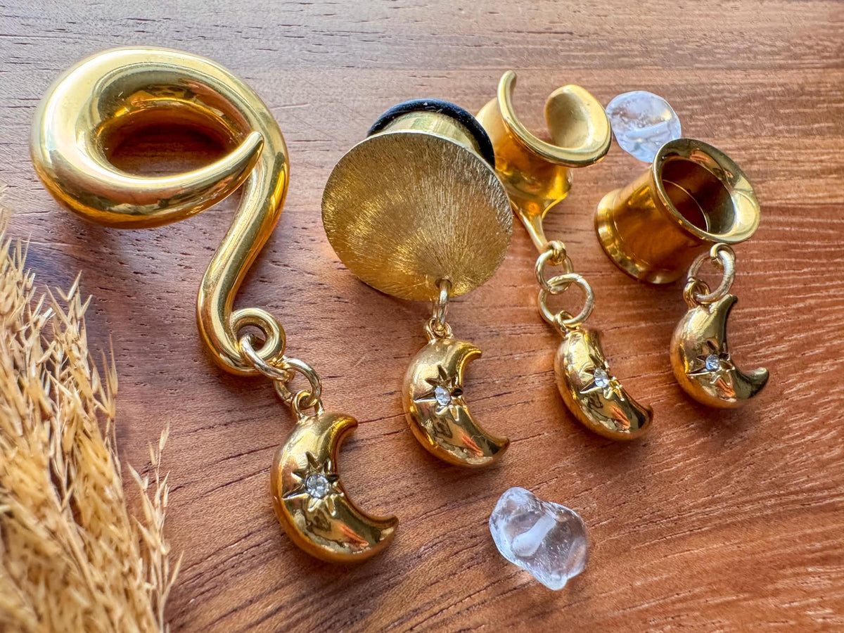 Mini gold crescent moon plug earrings with small celestial dangle charms for stretched ears.