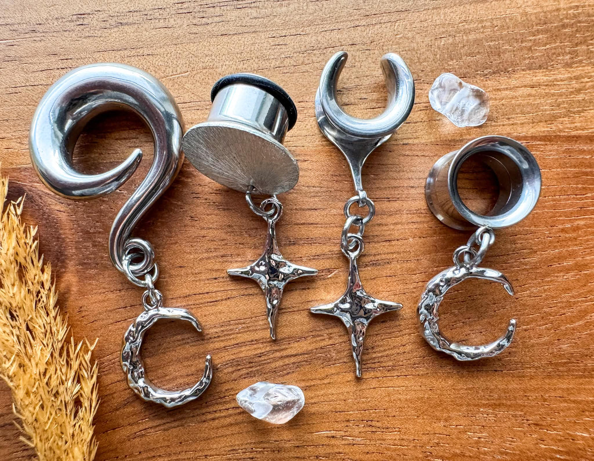 Mismatched star and moon plug earrings with dangling celestial charms for stretched ears.