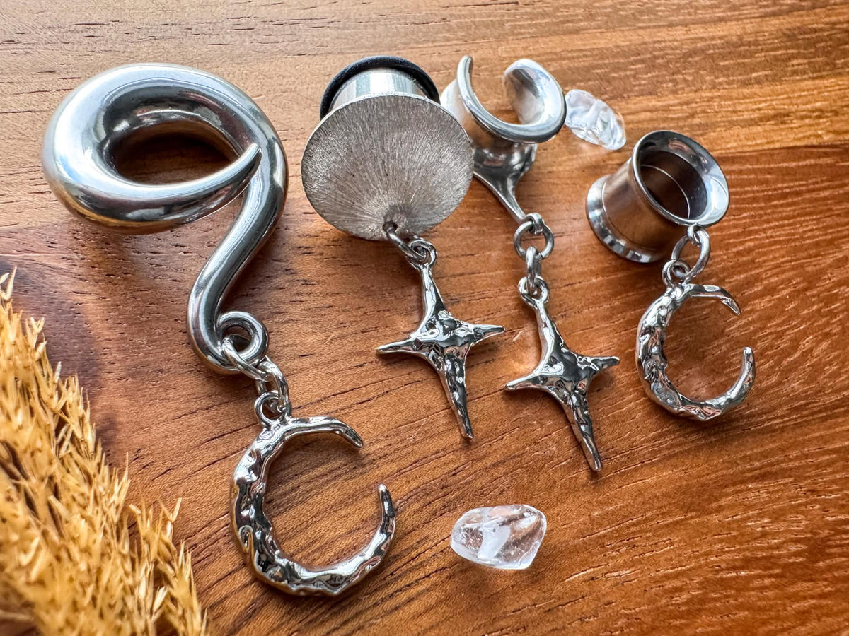 Mismatched star and moon plug earrings with dangling celestial charms for stretched ears.