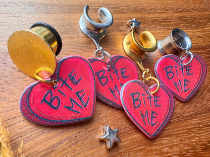 Red Bite Me heart plug earrings with bold heart-shaped dangling charms for stretched ears.