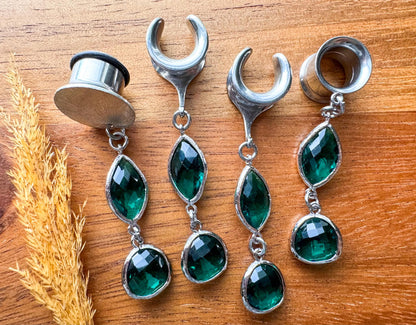 Silver plug earrings with emerald green accents and dangling details for stretched ears.