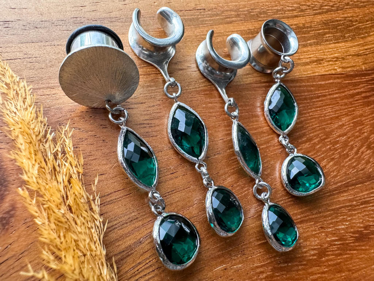 Silver plug earrings with emerald green accents and dangling details for stretched ears.