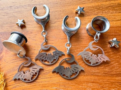 Silver stainless steel bat and crescent moon plug earrings with dangling celestial charms for stretched ears.
