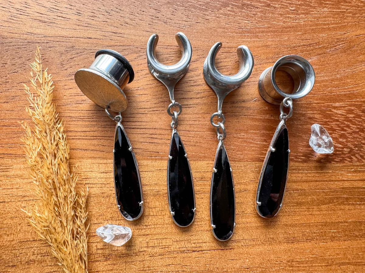 Black glass teardrop plug earrings with silver trim and dangling teardrop charms for stretched ears.