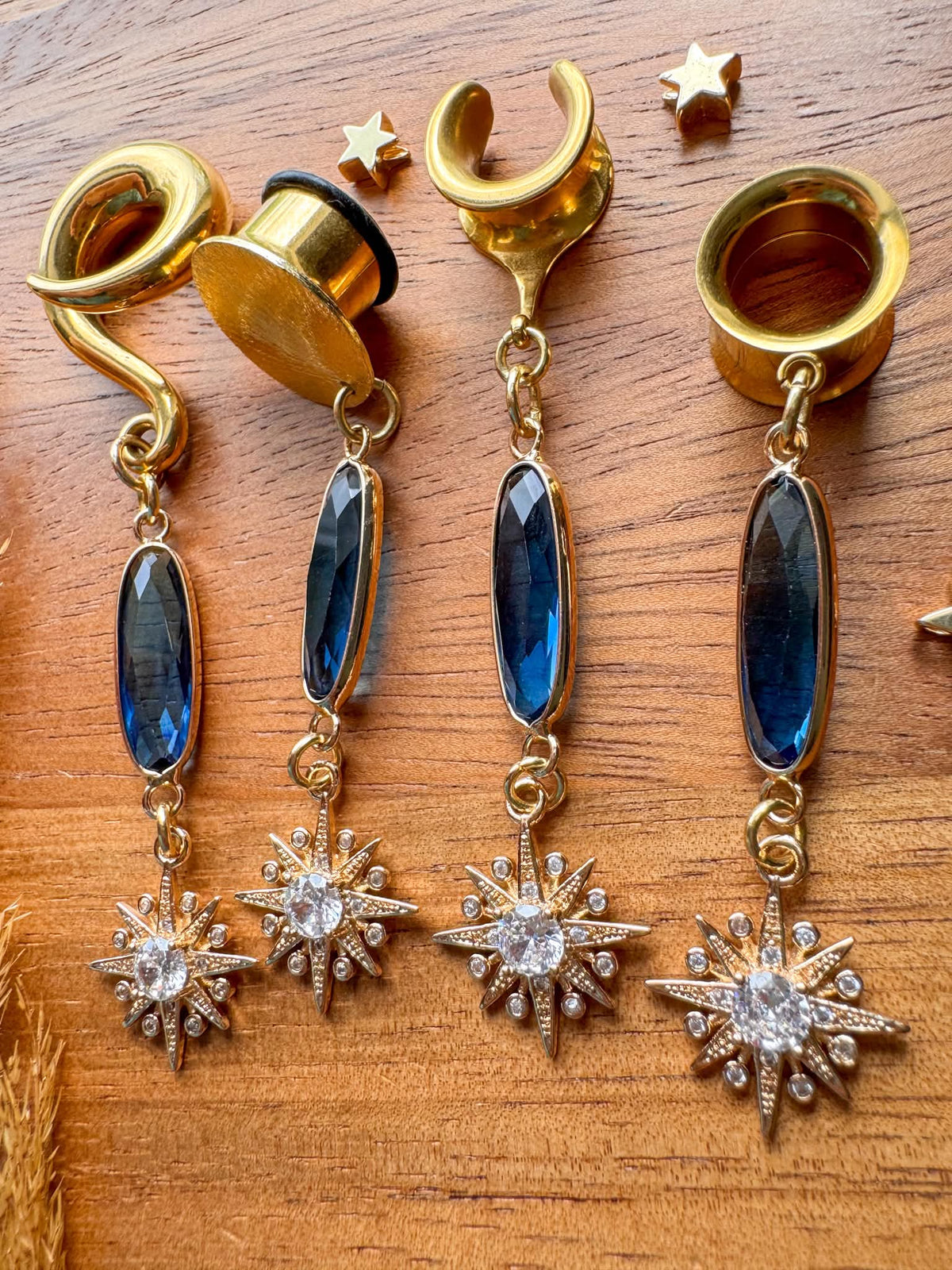 Gold plug earrings with deep blue faceted jewels and sparkling celestial starburst dangles for stretched ears.